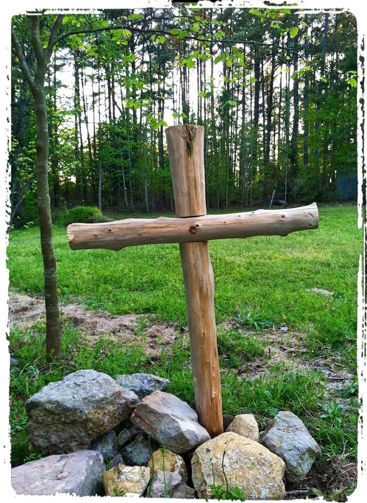 a wooden cross sitting on top of a pile of rocks in front of some trees