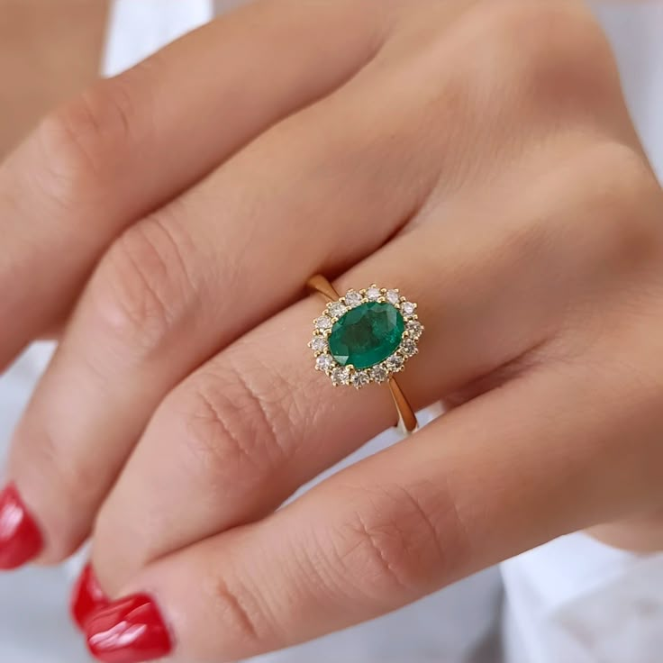 a woman's hand wearing a ring with an oval emerald and diamond halo setting