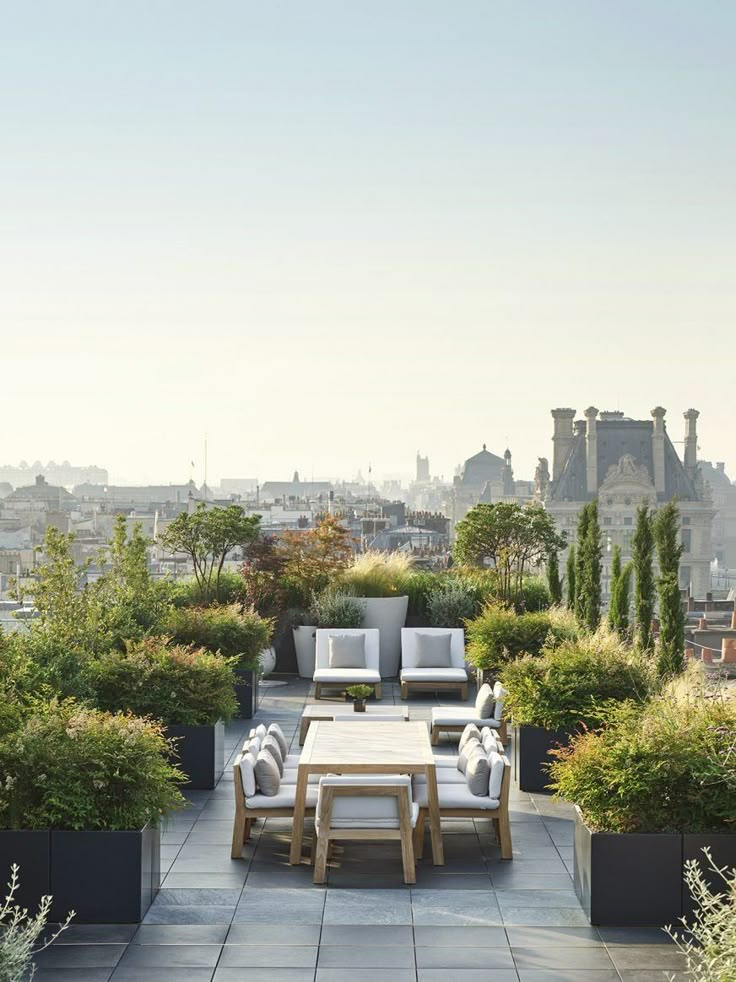 an outdoor seating area with potted plants and trees in the foreground, overlooking cityscape