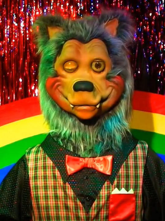 a man in a bear mask and bow tie standing next to a rainbow colored wall