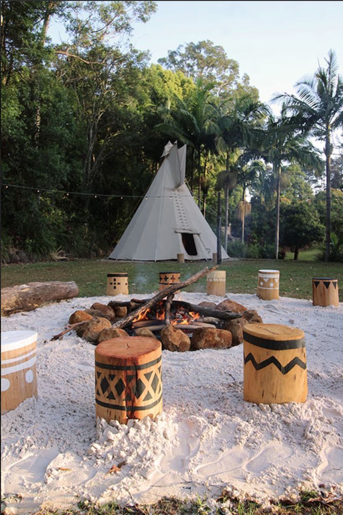 a teepee tent is in the background with fire pit and stools around it