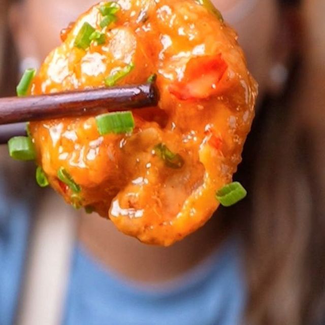 a woman holding up a piece of food with chopsticks