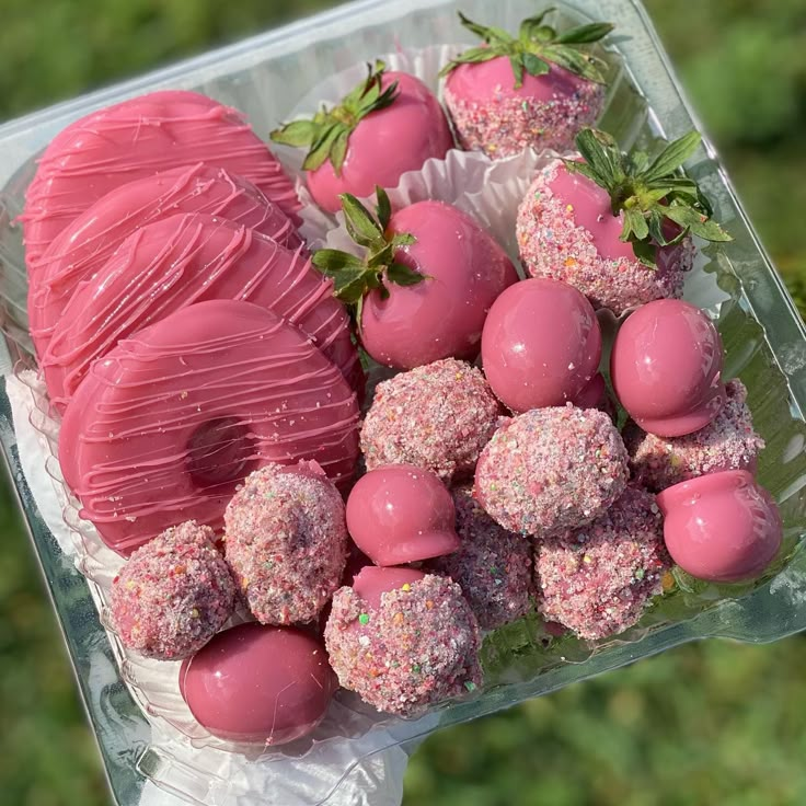 a plastic container filled with chocolate covered strawberries and other candy treats on top of a table