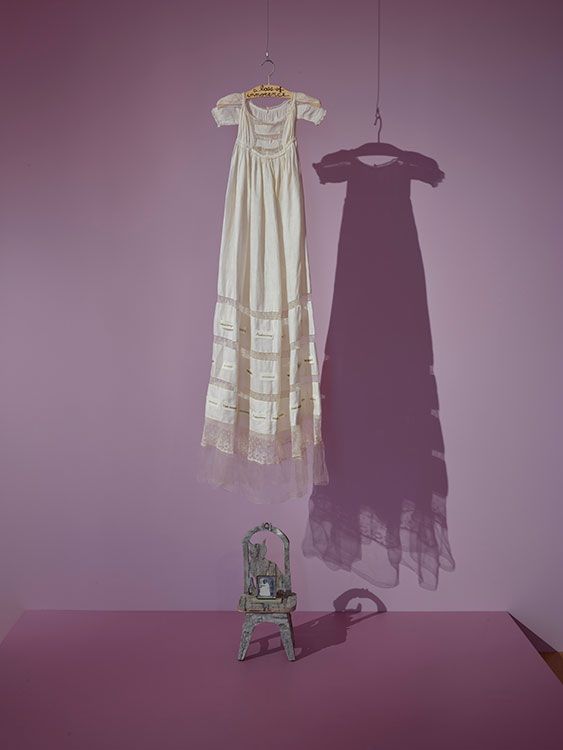 a white dress hanging on a purple wall next to a chair with a shadow cast on it