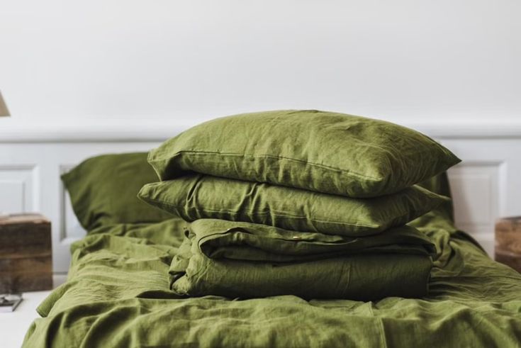 a pile of green linens on top of a bed next to a night stand