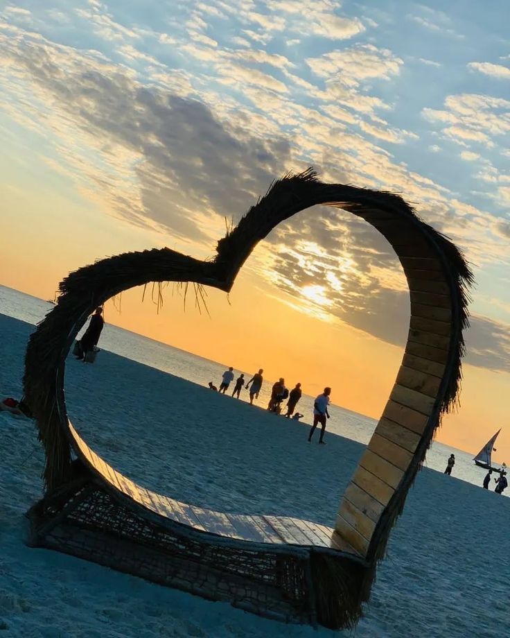 a heart shaped sculpture on the beach at sunset