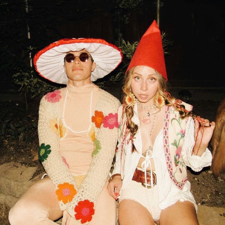 two people dressed in costumes and hats sitting on the ground with an animal behind them