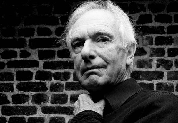 black and white photograph of an older man in front of a brick wall with his hands on his chest