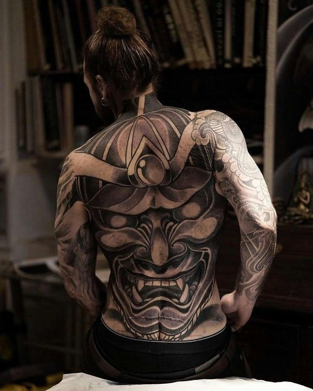 a woman with tattoos on her back is sitting in front of a bookshelf