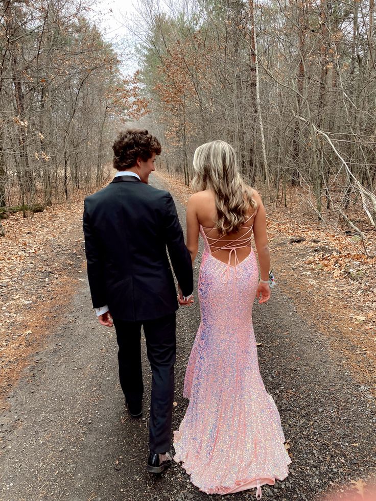 a man and woman walking down a path in the woods holding hands while wearing formal attire