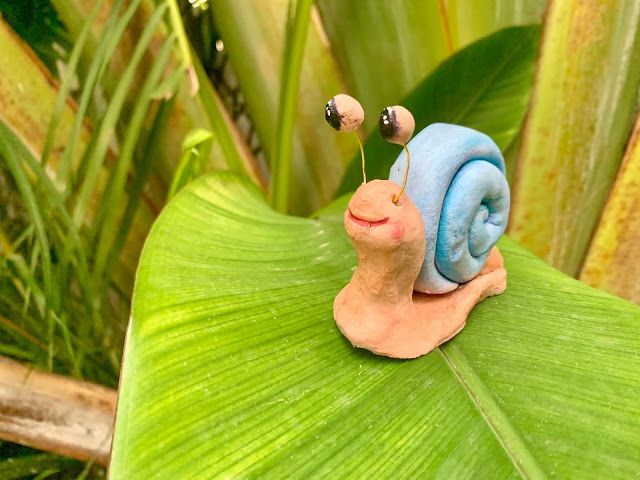 a snail figurine sitting on top of a green leaf