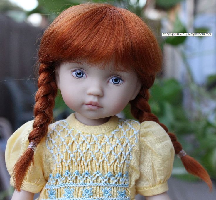 a close up of a doll with red hair and blue eyes wearing a yellow dress