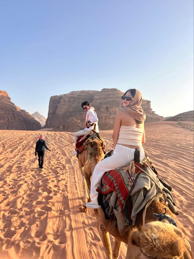 three people are riding camels in the desert