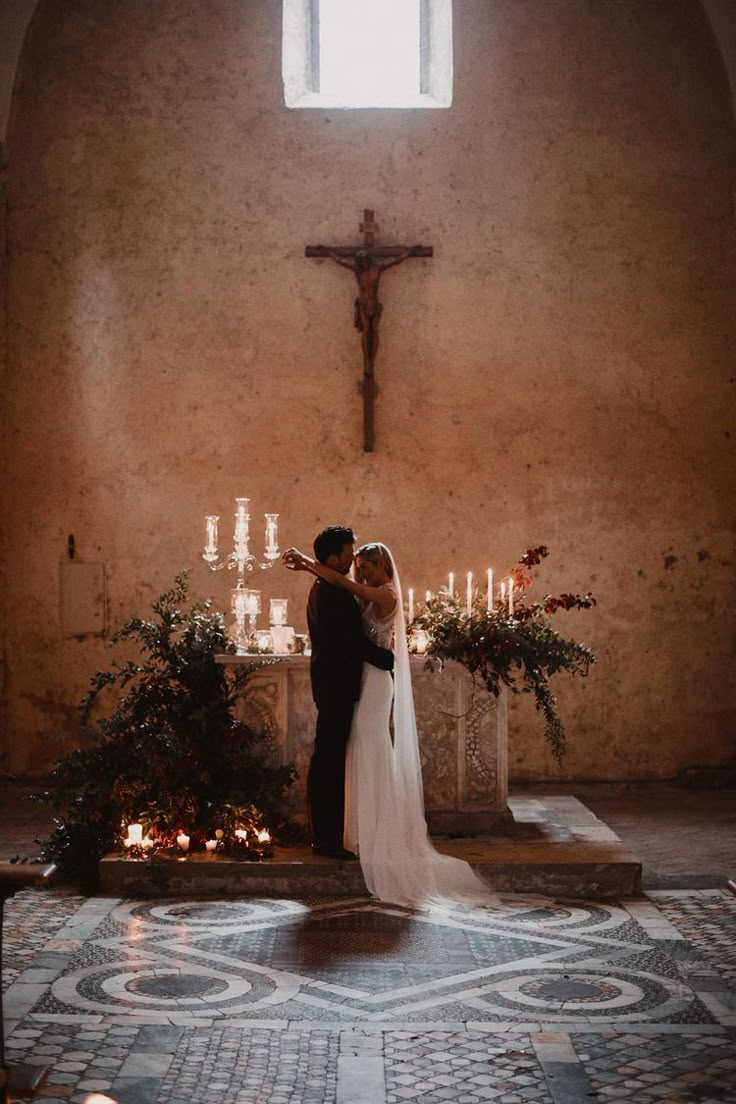 a man and woman standing in front of a cross with candles on the altar behind them