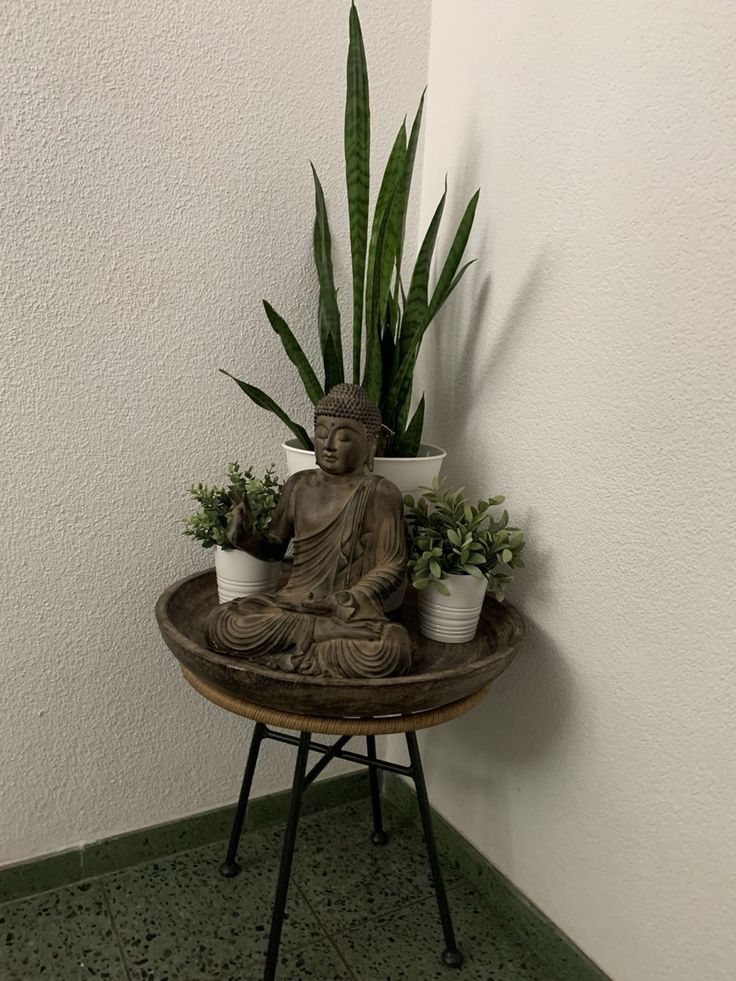 a buddha statue sitting on top of a table next to potted plants and a planter