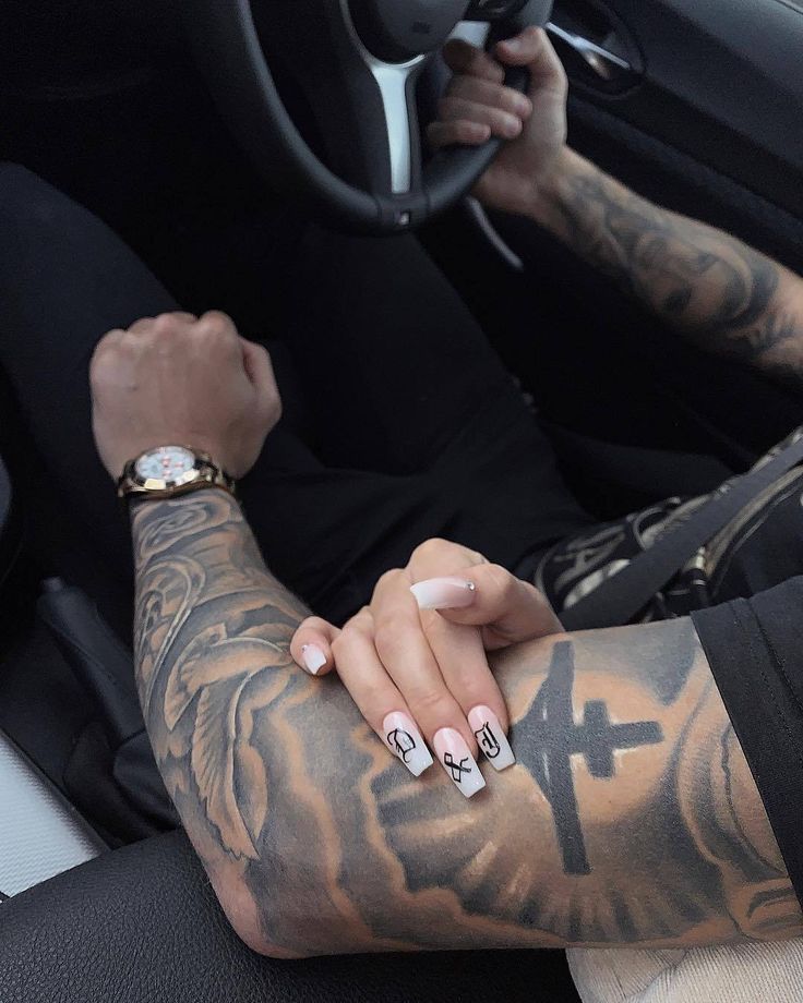 a man with tattoos on his arm and wrist sitting in the driver's seat of a car