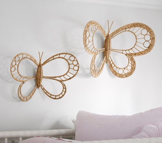 two decorative butterfly wall hangings on the wall next to a crib with pink pillows