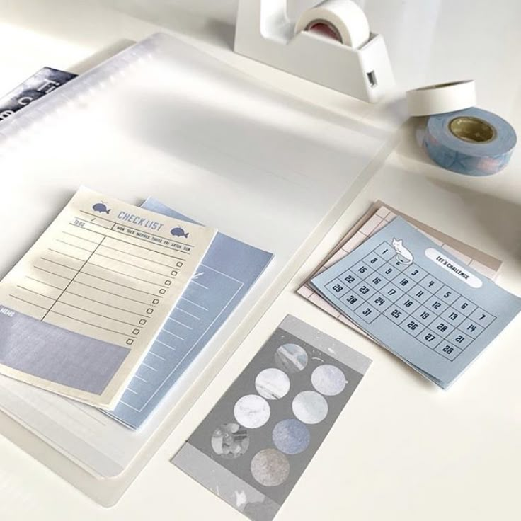 a white desk topped with lots of papers and stickers next to a roll of tape