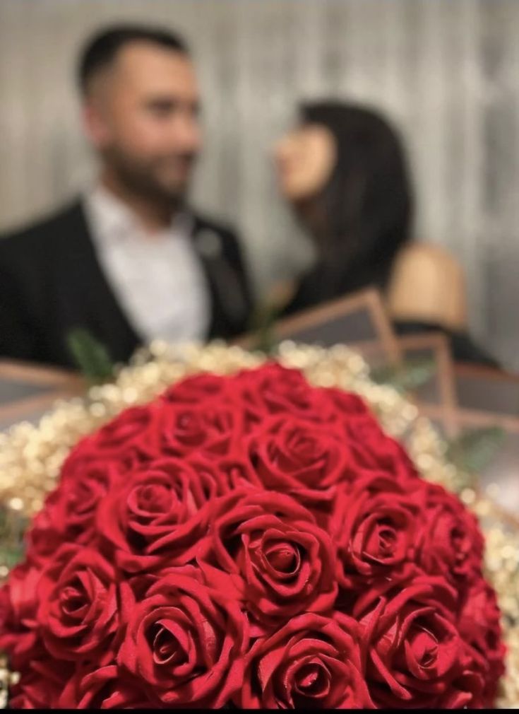 a bouquet of red roses sitting on top of a table next to a man in a tuxedo