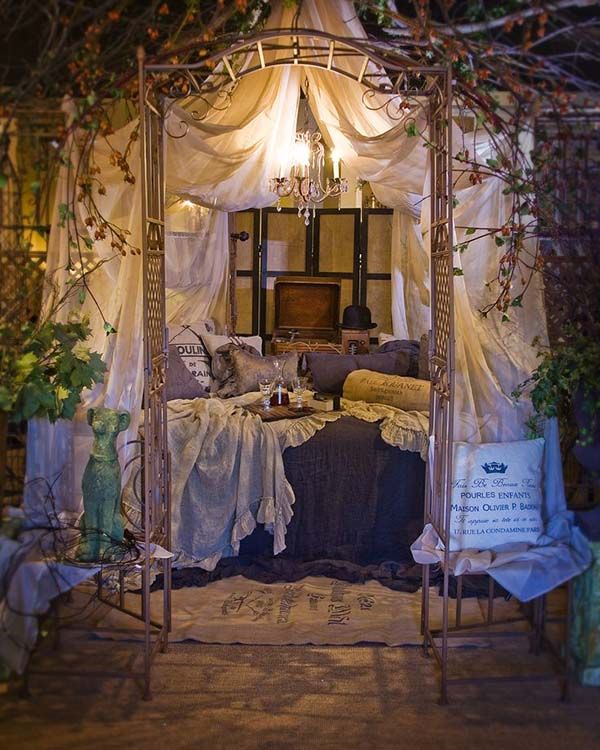 a canopy bed with curtains and pillows in a room filled with greenery on the walls