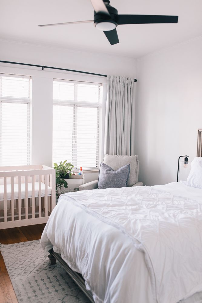 a white bed sitting in a bedroom next to a window with blinds on it's sides