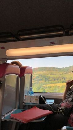 a man sitting on a train next to a window with mountains in the back ground