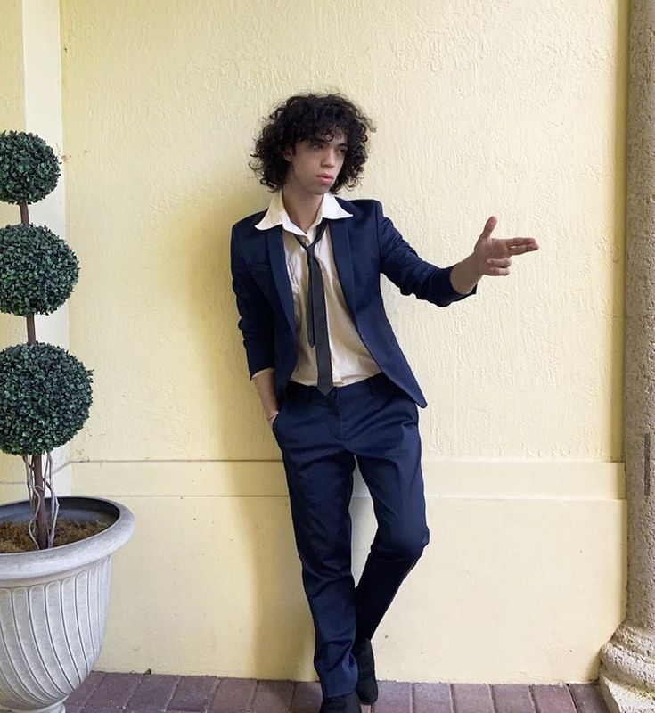 a man in a suit and tie leaning against a wall with his hand out to the side