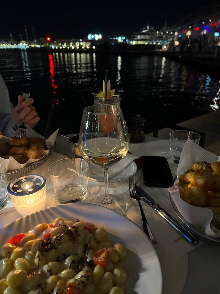 two plates of food on a table with wine and water in the background at night