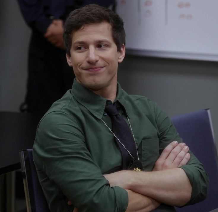 a man sitting in a chair with his arms crossed and looking at the camera while smiling