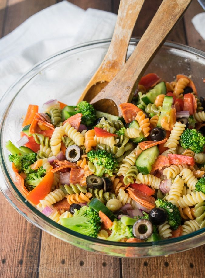 a glass bowl filled with pasta salad on top of a wooden table