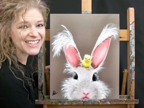 a woman is smiling next to an easel with a painting of a white rabbit