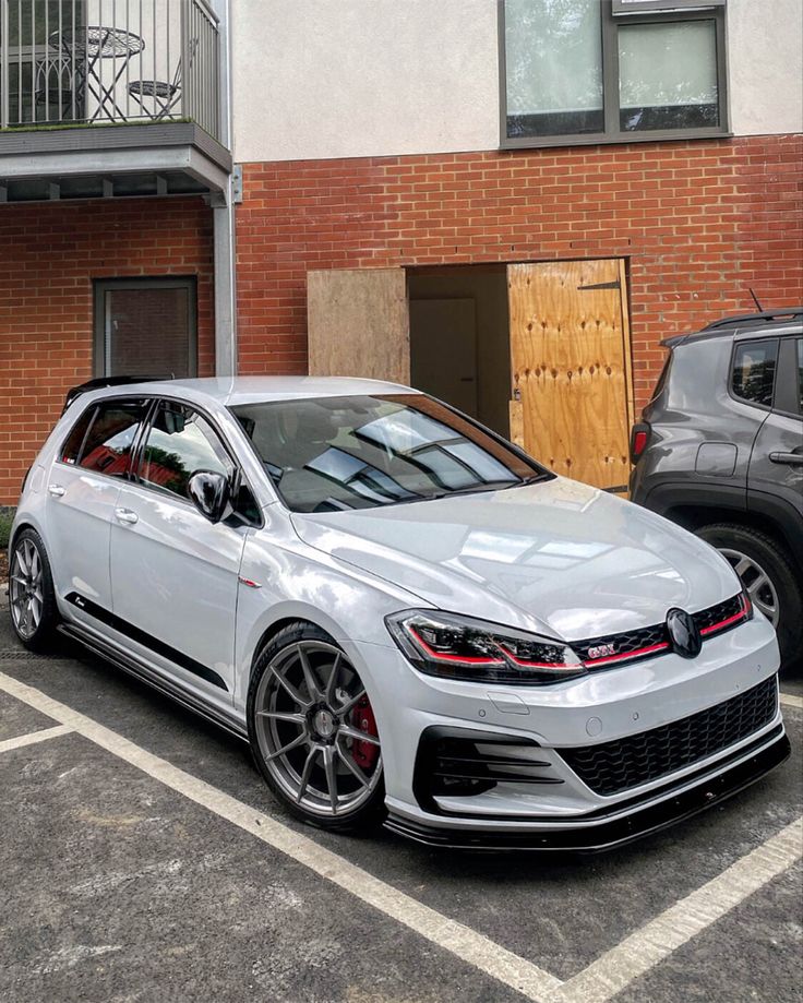 a white car parked in front of a brick building next to two other black cars