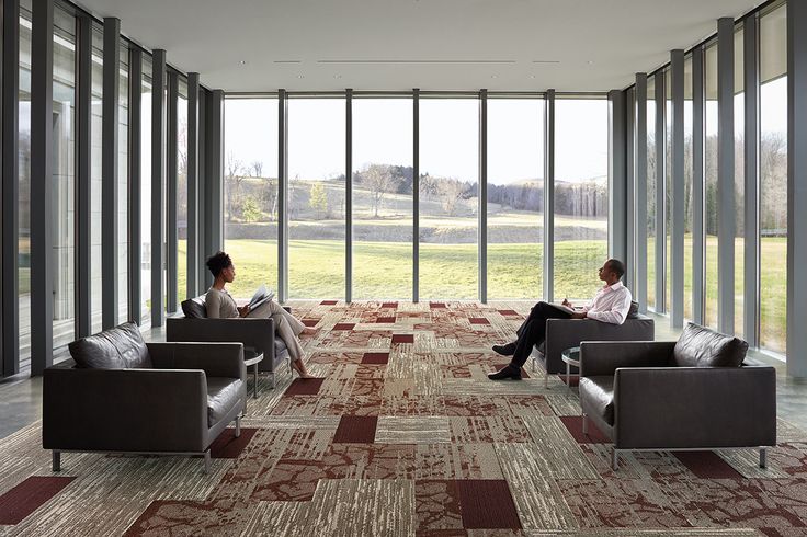 two people sitting on couches in a room with large glass walls and floor to ceiling windows