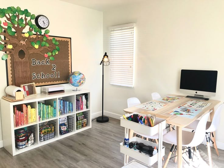 a room with a desk, bookshelf and school supplies on the floor in front of a chalkboard