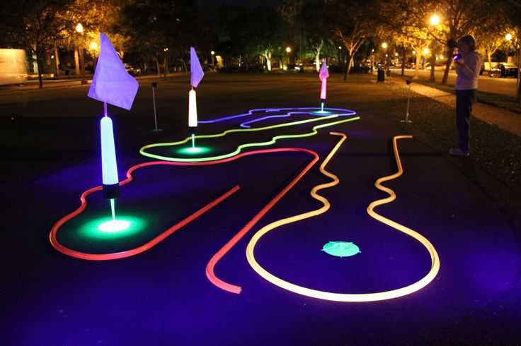 an illuminated pathway in the middle of a park at night with people standing around it