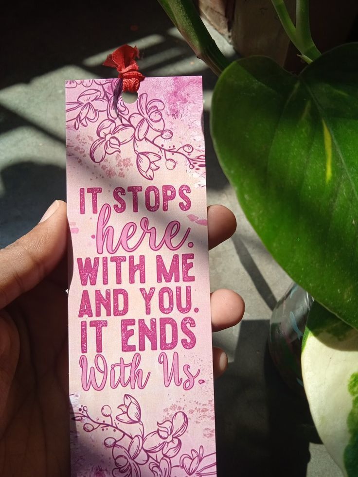 a person holding up a pink bookmark that says, it stops here with me and you'll ends with us