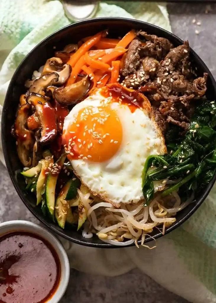 a bowl filled with meat, veggies and an egg on top of it