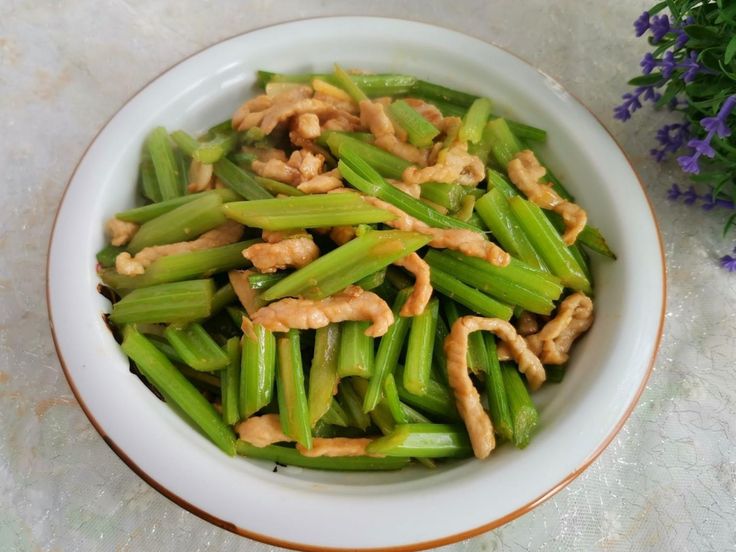 a white bowl filled with green beans covered in peanut sauce and some flowers next to it