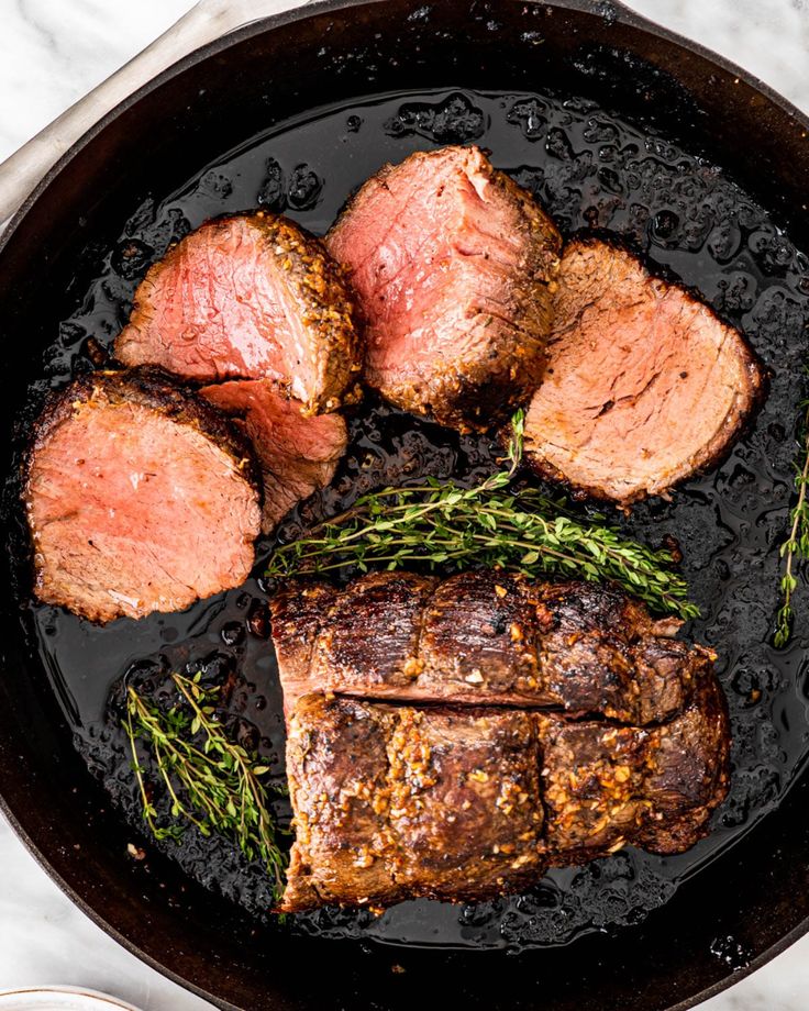 steaks and potatoes cooking in a skillet on a marble counter top, with rosemary sprigs