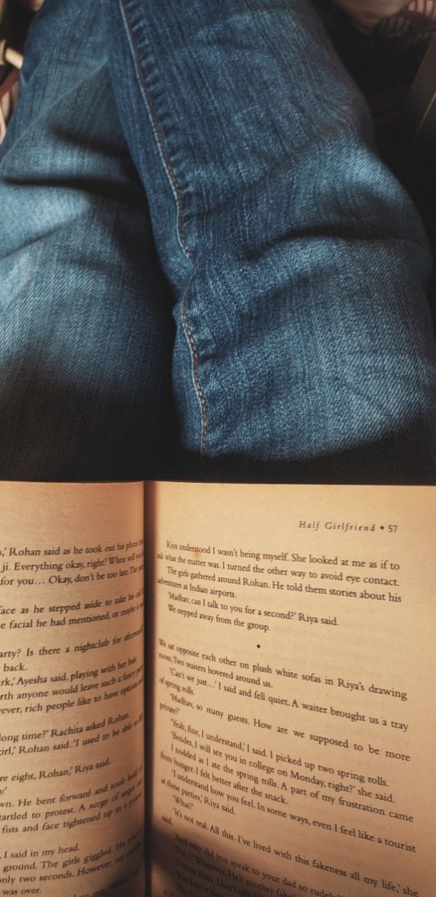 an open book sitting on top of a person's lap next to a pair of jeans