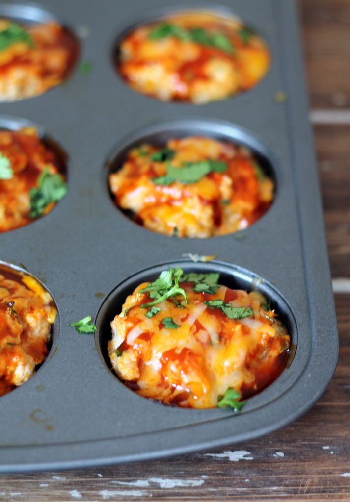 a muffin tin filled with mini pizzas on top of a wooden table next to a white wall