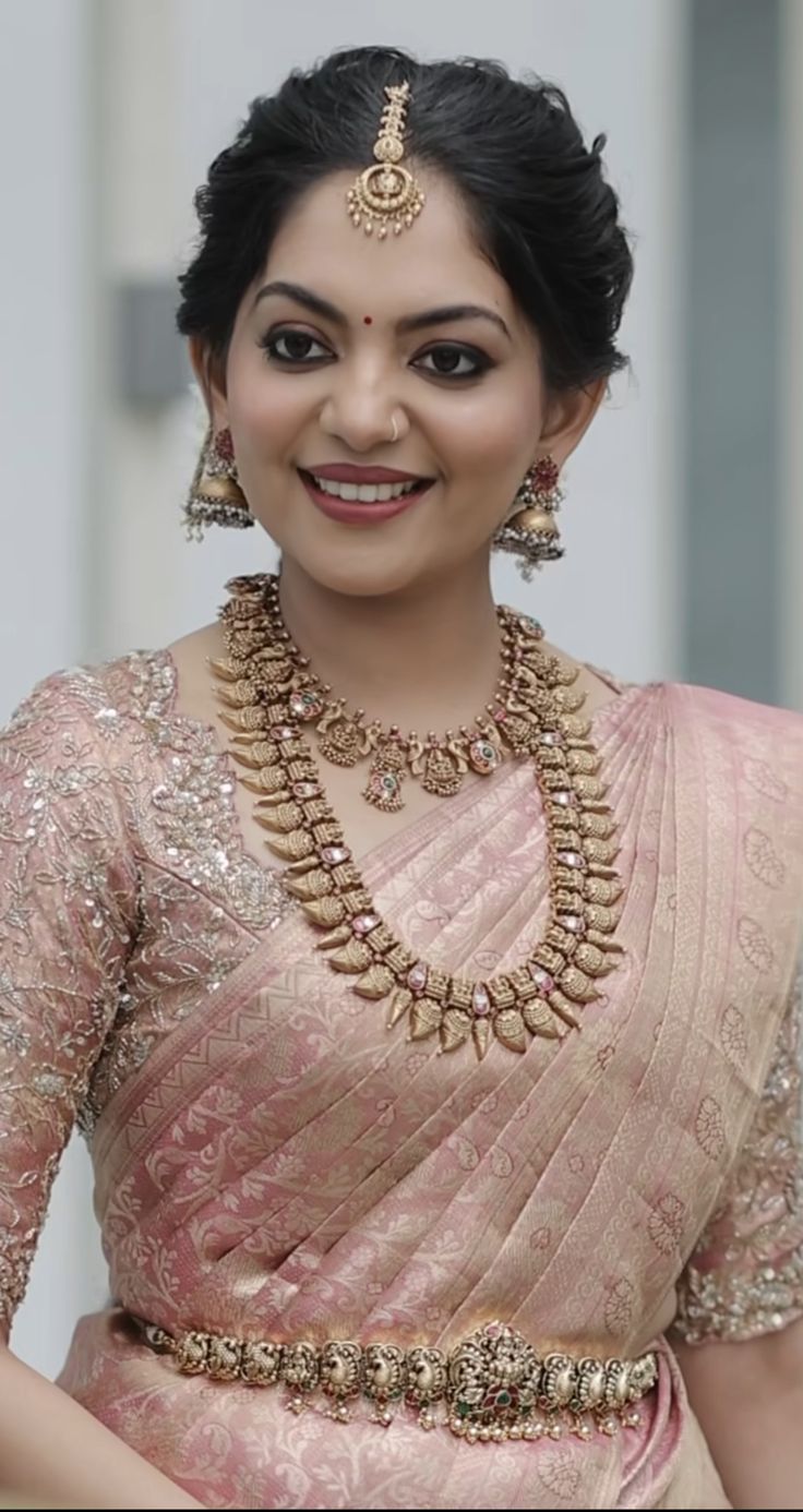 a woman in a pink sari with gold jewelry on her neck and shoulder, smiling