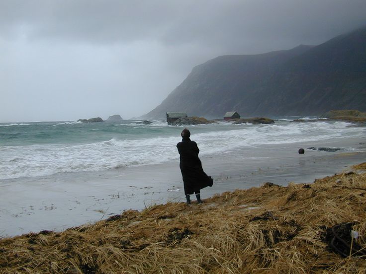 a woman standing on top of a sandy beach next to the ocean in black and white