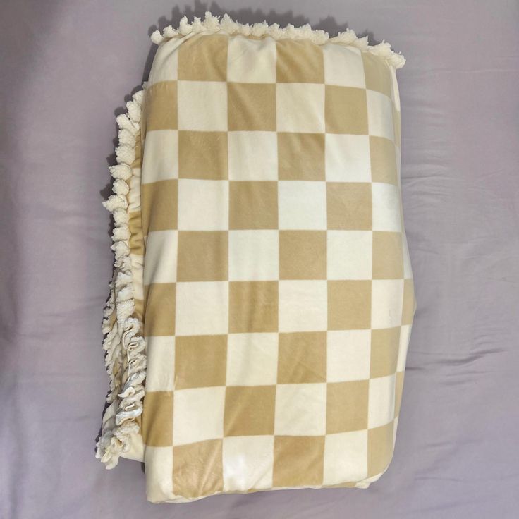 a brown and white checkered blanket laying on top of a purple bed sheet with tassels