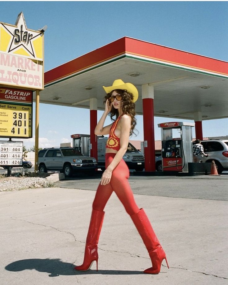 a woman wearing red boots and a cowboy hat walks in front of a gas station