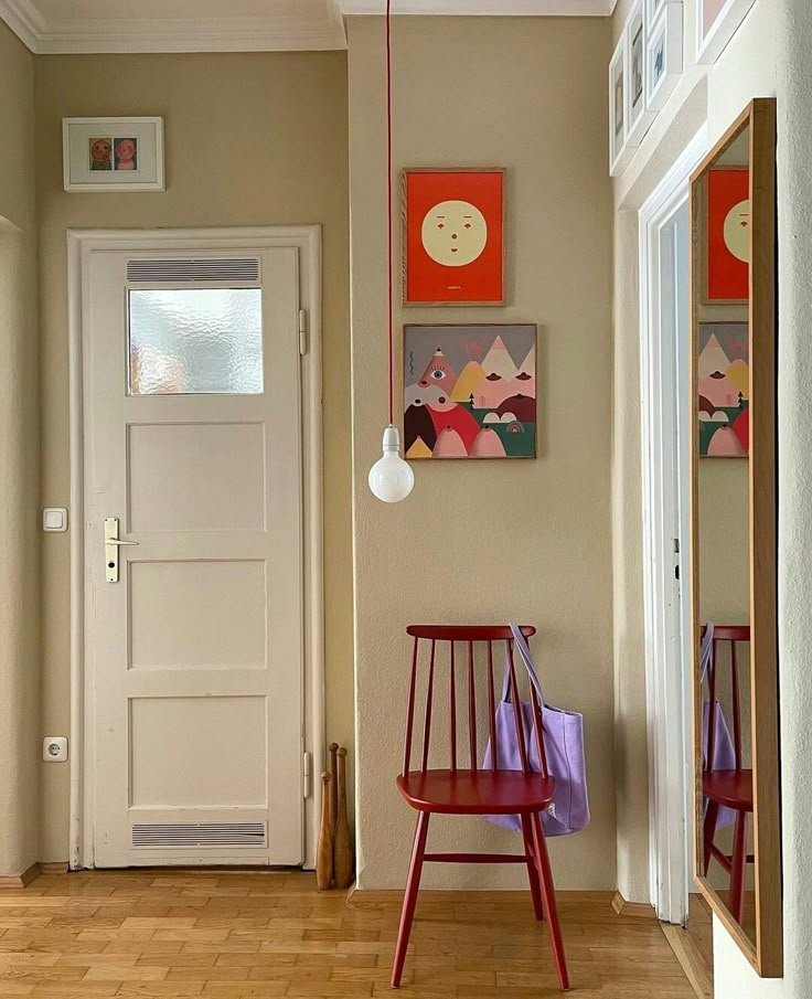 a room with two chairs and paintings on the wall next to a white door that leads to a hallway