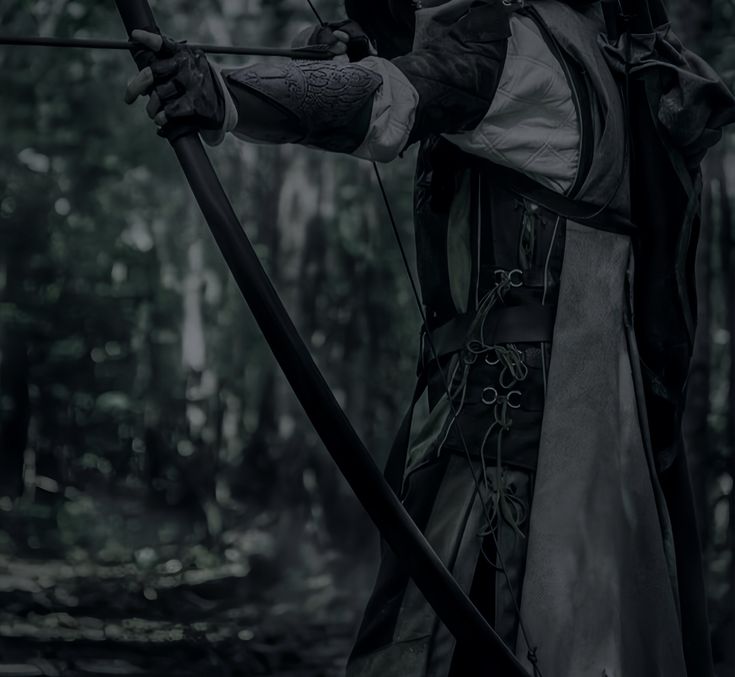 a man dressed in medieval clothing holding a bow and arrow while standing in the woods