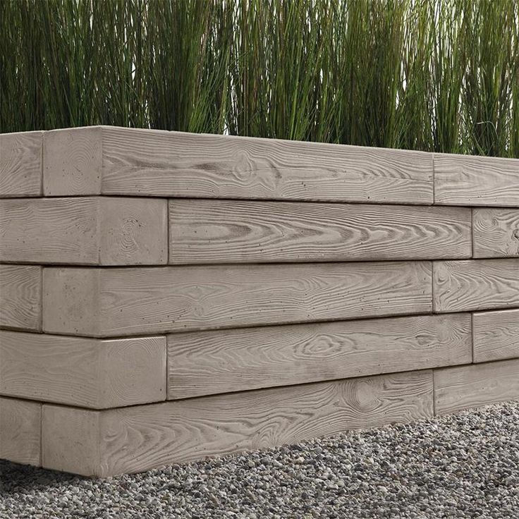 a wooden planter sitting on top of gravel next to tall green plants and grass