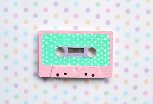 a pink and green wooden toy cassette on a polka dot wallpapered background with white dots