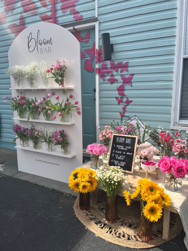 flowers are on display in front of a blue building with pink and yellow flowers hanging from it's sides